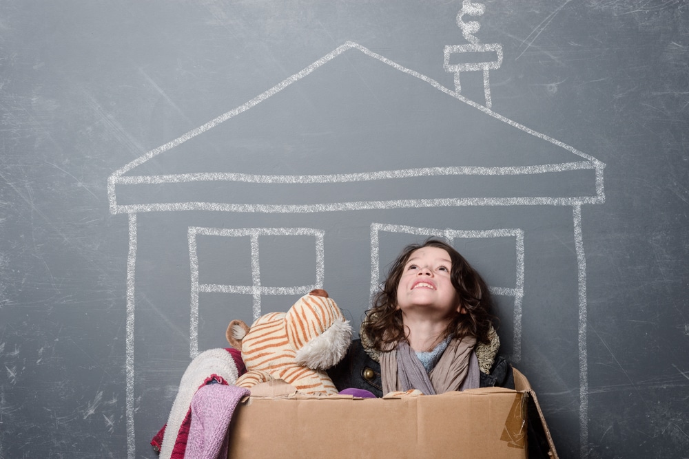 Shabby little girl in cardboard box dreaming of home