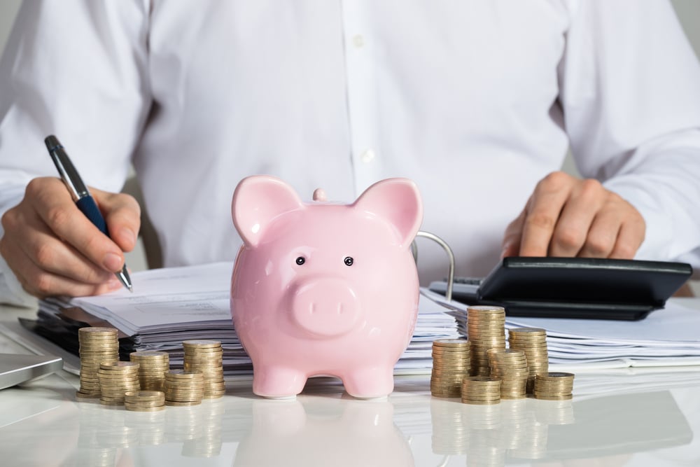 Businessman doing accounts behind piggy bank and piles of coins