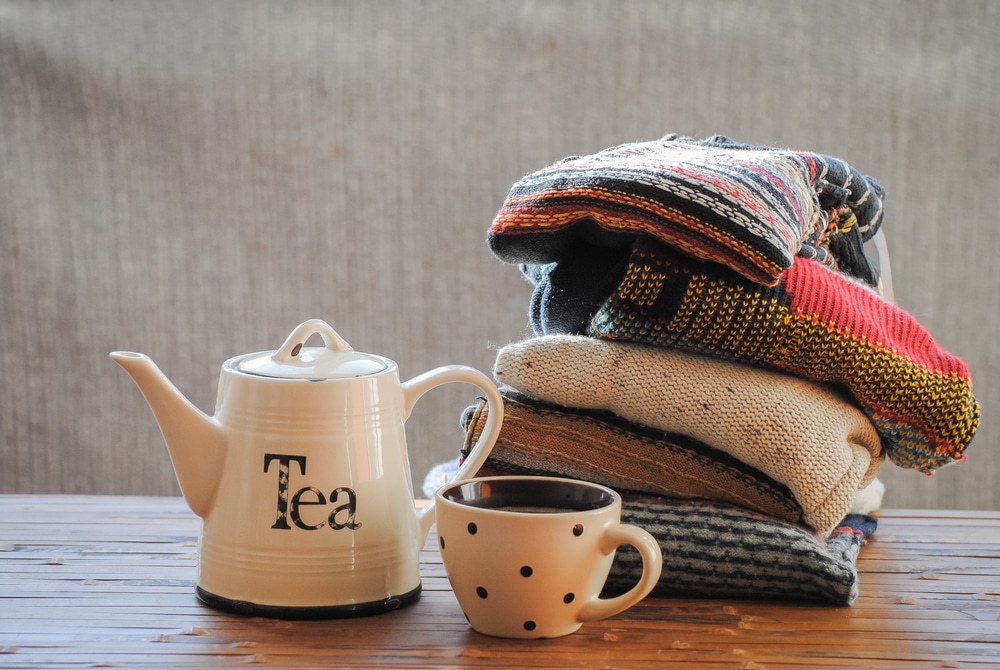 Tea pot and cup beside pile of kitted wooly jumpers